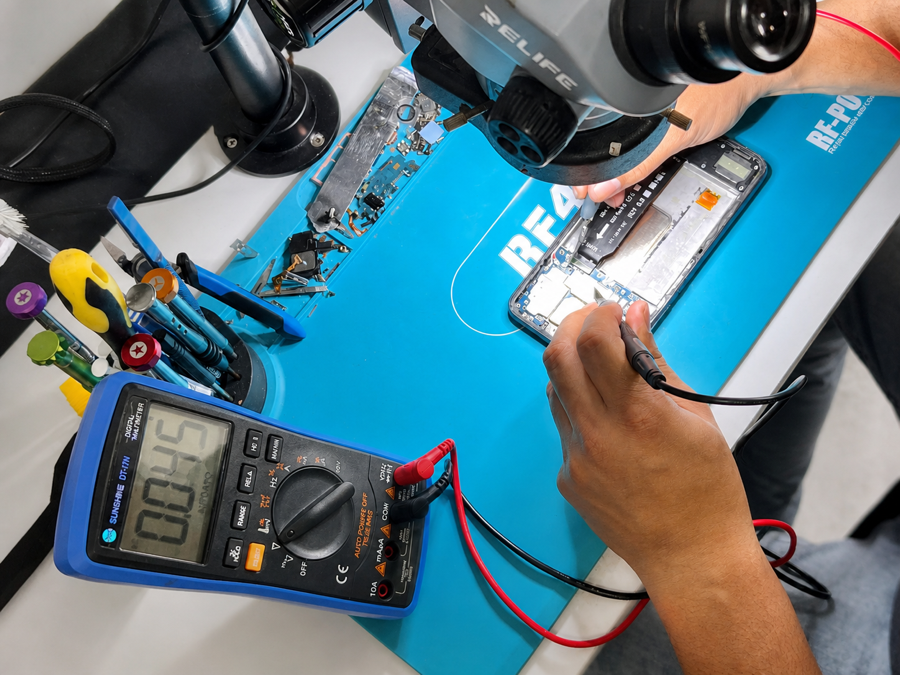 Técnico realizando diagnóstico em celular com microscópio e multímetro